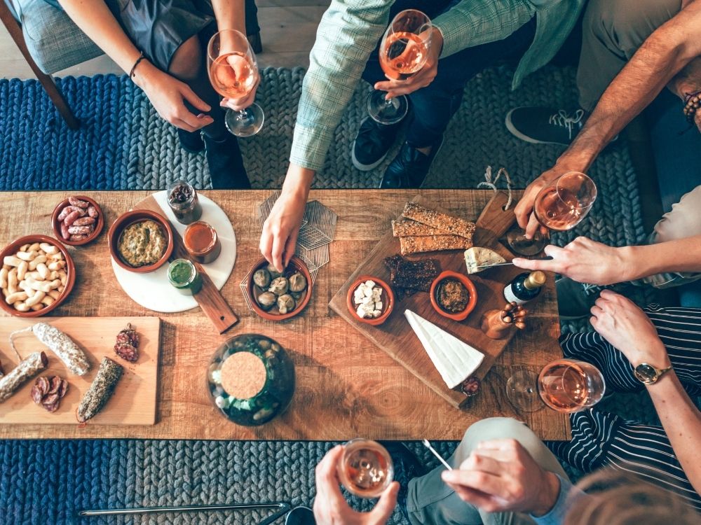 Top shot of peoples hands reaching out for charcuterie board items while sipping on wine.
