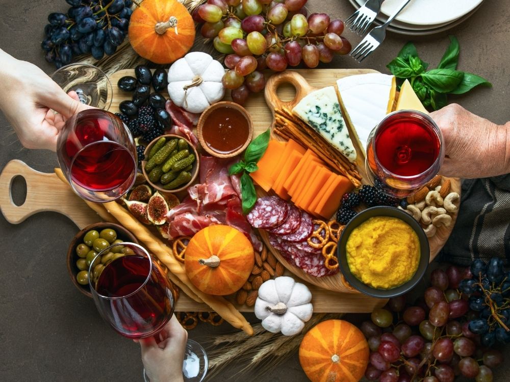 Top down view of people raising their red wine glasses over a fall inspired charcuterie board