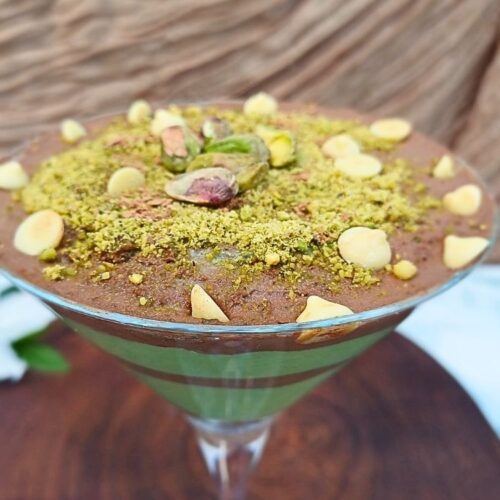 Dubai chocolate dessert inspired cottage cheese mousse with layers of rich dark chocolate and green pistachio cream swirls topped with pistachios and white chocolate chips in a martini glass.