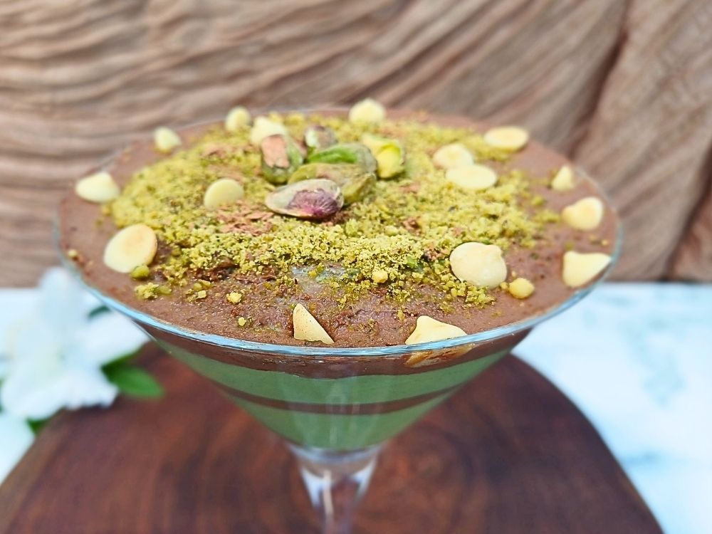 Dubai chocolate dessert inspired cottage cheese mousse with layers of rich dark chocolate and green pistachio cream swirls topped with pistachios and white chocolate chips in a martini glass.