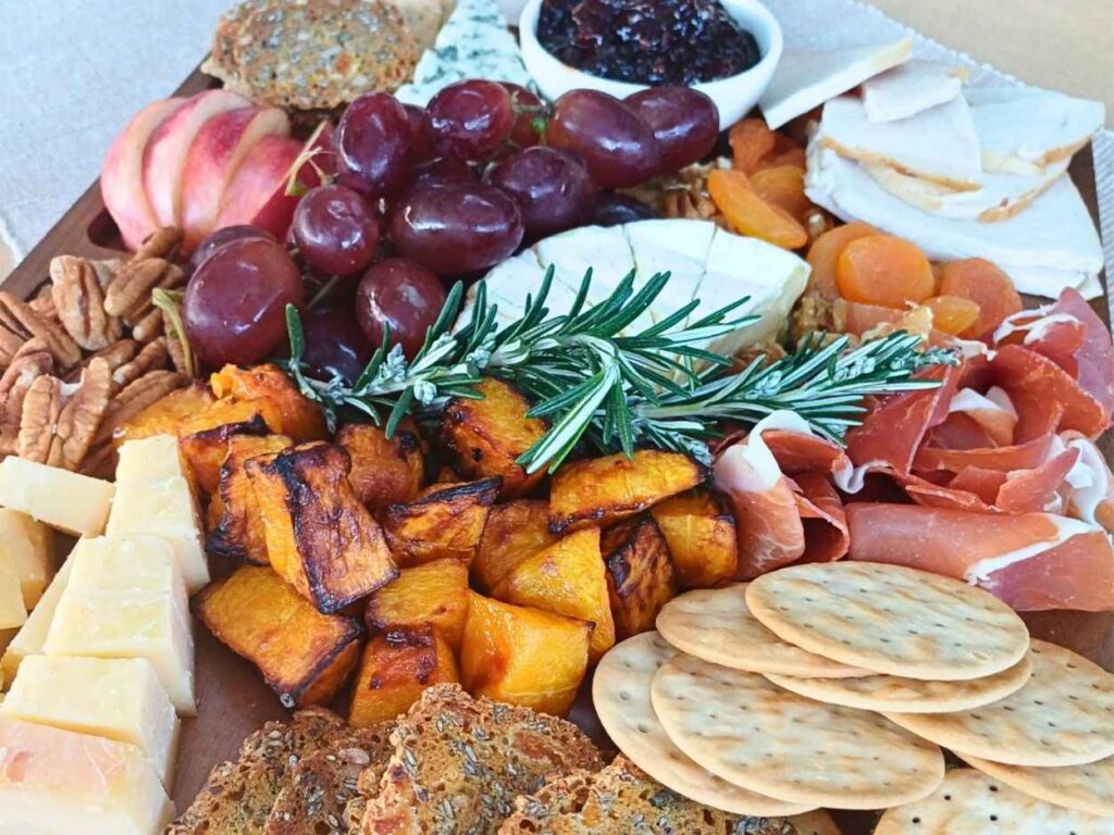 simple thanksgiving charcuterie board with turkey, cranberry sauce, roasted pumpkin, crackers and cured meats with cheeses