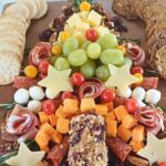 Christmas tree charcuterie board made of cured meats, cheeses and fruit decorated with rosemary springs on a wooden board