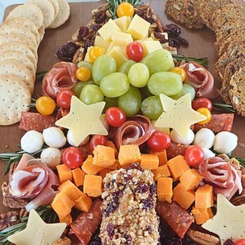 Christmas tree charcuterie board made of cured meats, cheeses and fruit decorated with rosemary springs on a wooden board