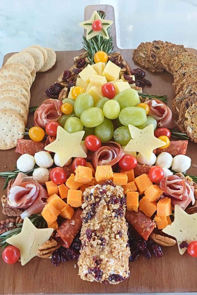 Christmas tree charcuterie board made of cured meats, cheeses and fruit decorated with rosemary springs on a wooden board