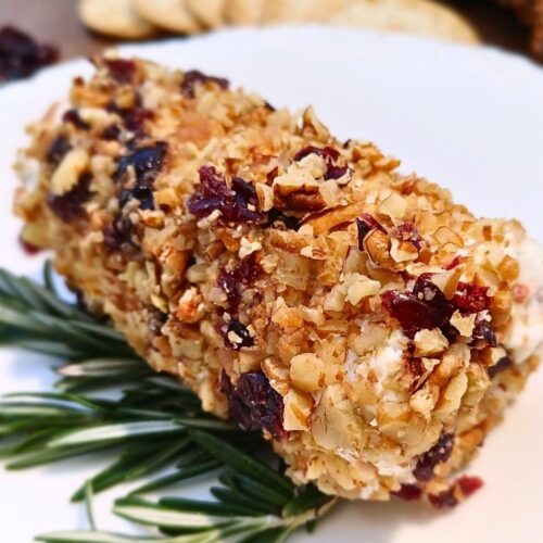 Cranberry pecan goat cheese appetizer log on a white plate with rosemary strings as a decoration under the goat cheese log