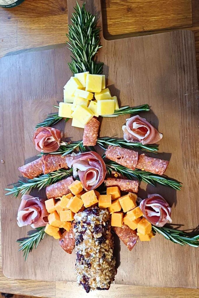 Rosemary springs, goat cheese log and cured meats laid out in a Christmas tree shape on a charcuterie board