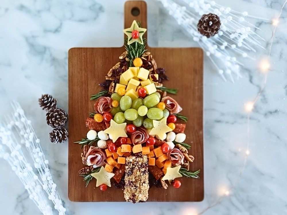 A Christmas tree shaped charcuterie board with variety of cured meats, cheeses and fruit place on a wooden board
