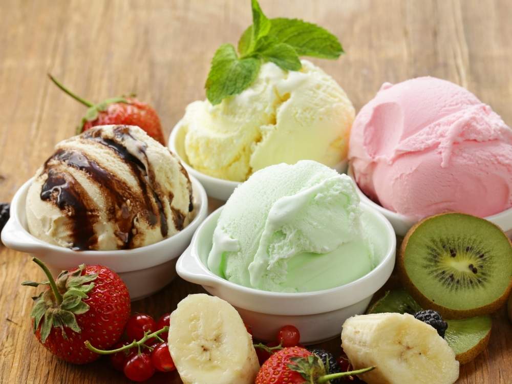 Four servings of various flavors of dairy free Ninja Creami ice cream with fresh fruit surrounding the bowls