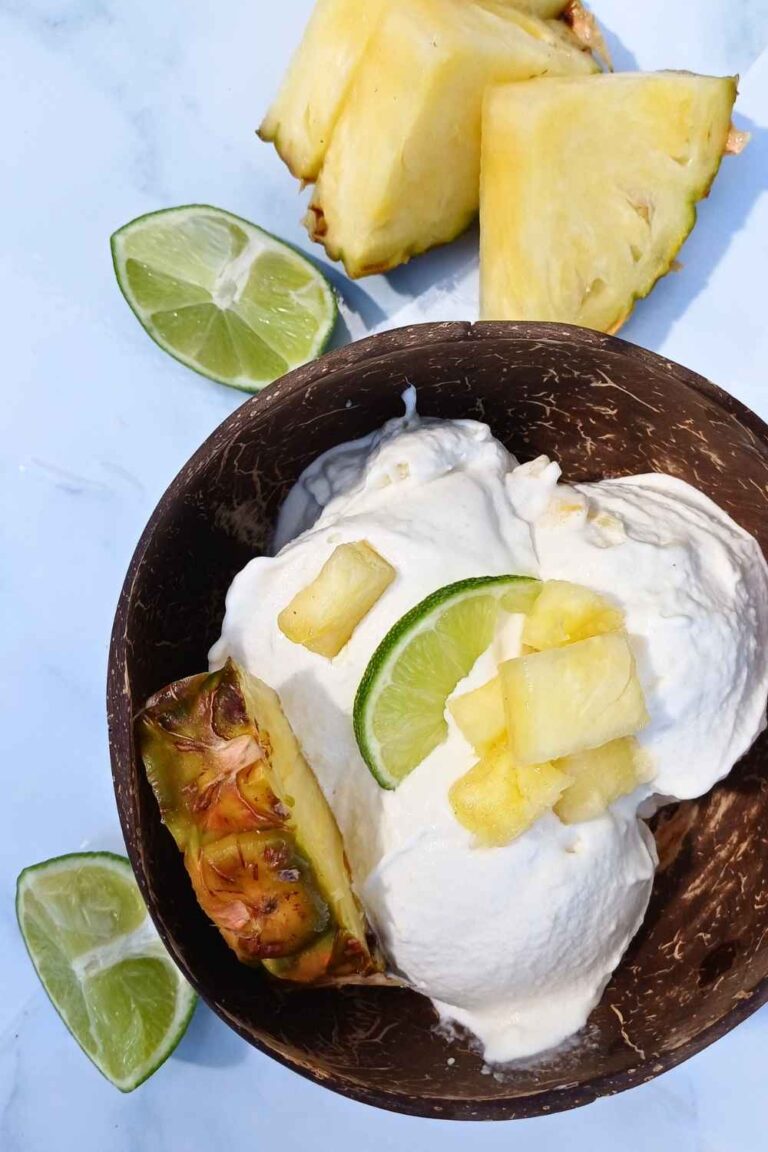 Pineaple, coconut and lime Ninja Creami vegan ice cream in a coconut shell bowl with wedges of lime and pineaple around