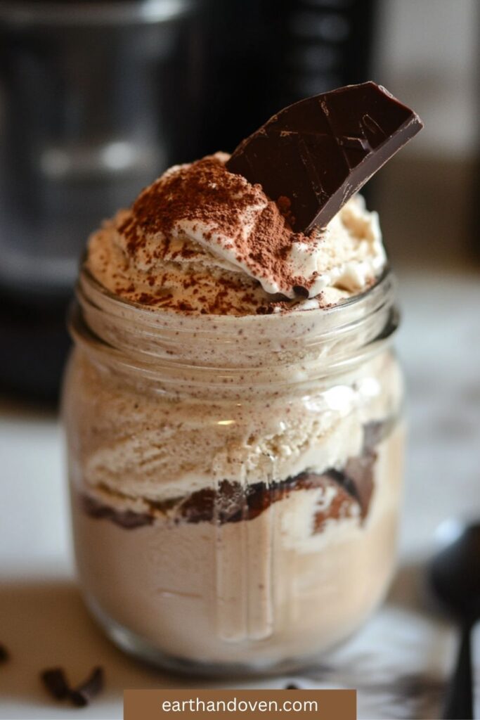 Chocolate ice cream in a glass jar topped with pieces of dark chocolate and whipped cream