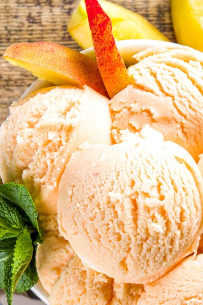 Scoops of peach flavored frozen yogurt in a bowl with slices of fresh peaches