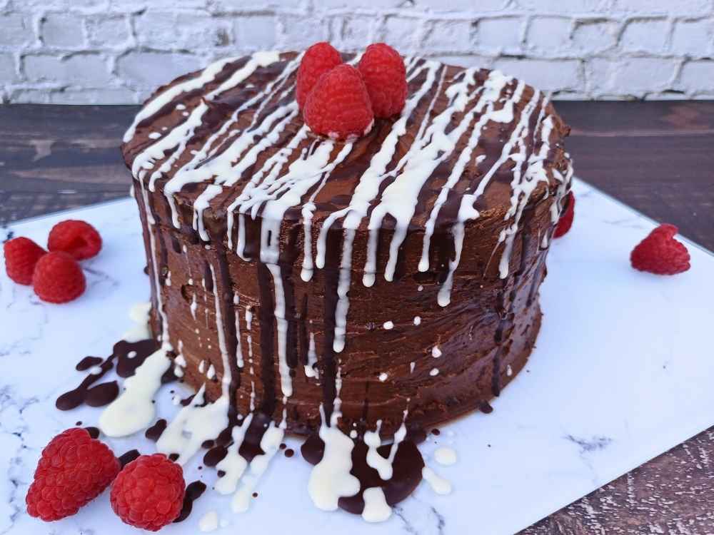 Chocolate cake decorated with raspberries and white chocolate drizzle