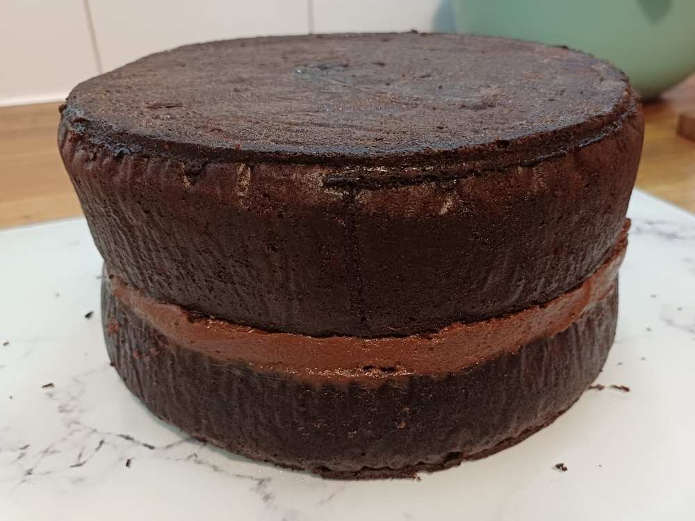 layered chocolate cake unfinished showing only first layer of frosting added