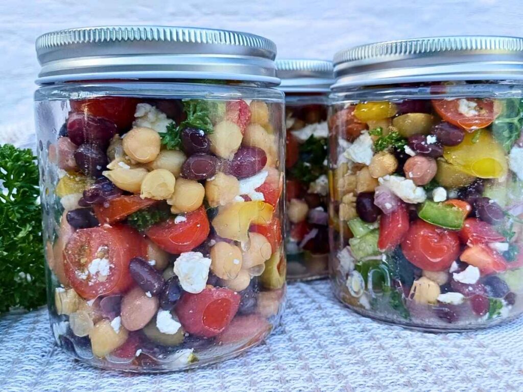 Glass jars of dense bean salad with vegetables for meal prep
