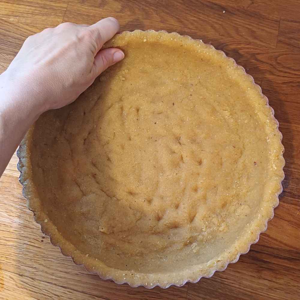 Hand showing how to shape almond flour dough into a pie dish
