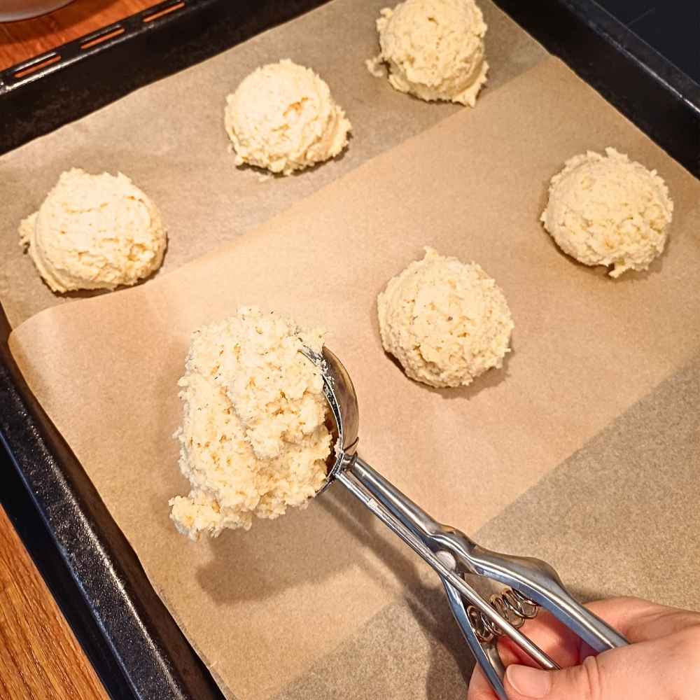 Scooping almond flour biscuit batter on to a baking tray with ice cream scoop