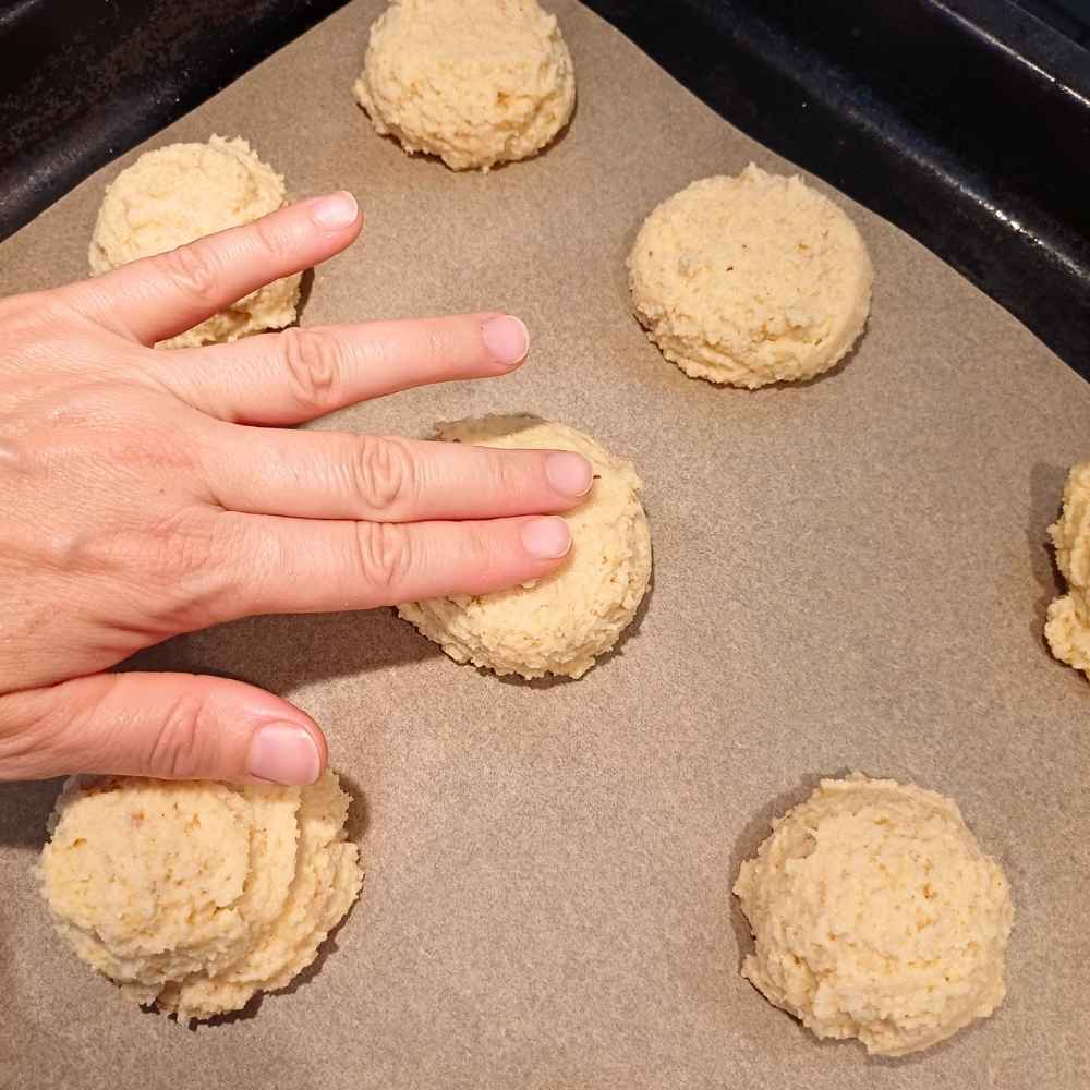 Hand pressing down on almond flour biscuits to flatten them before baking