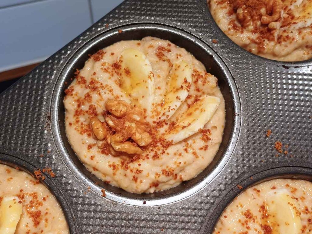 A muffin tin filled with batter for almond flour banana muffins with nuts