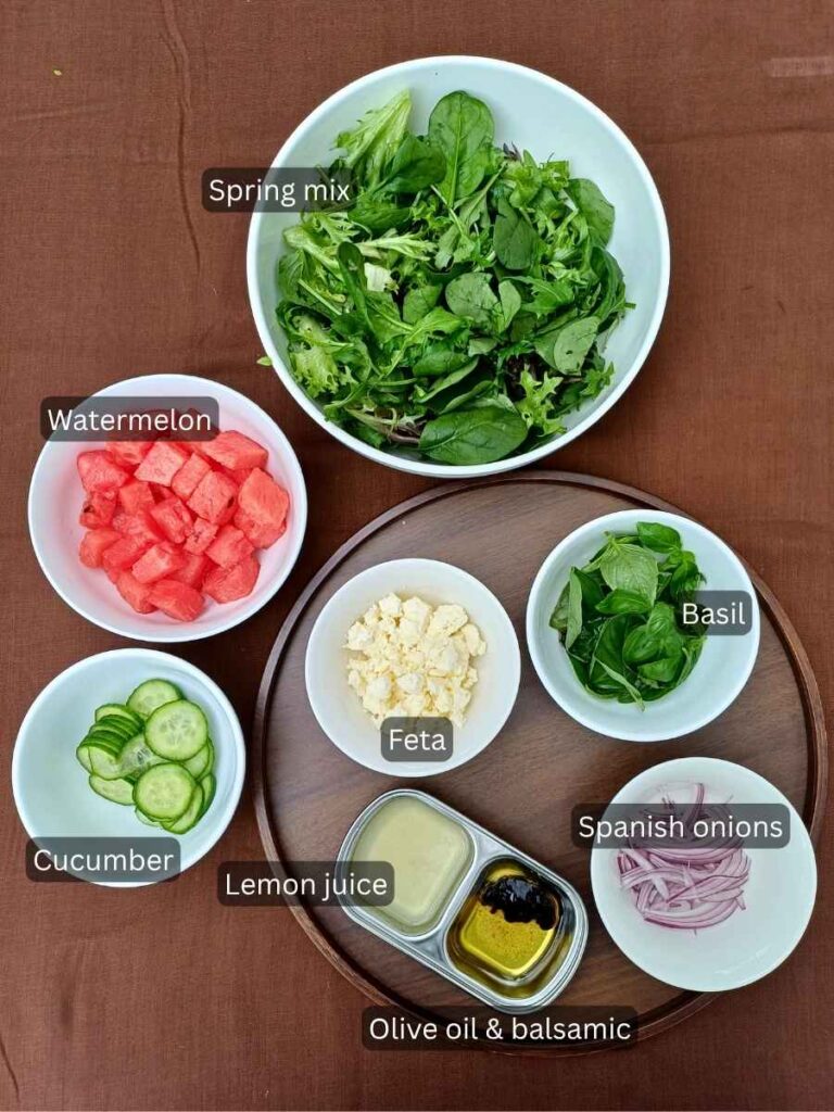 Ingredients for watermelon feta salad with spring mix and basil laid out in bowls