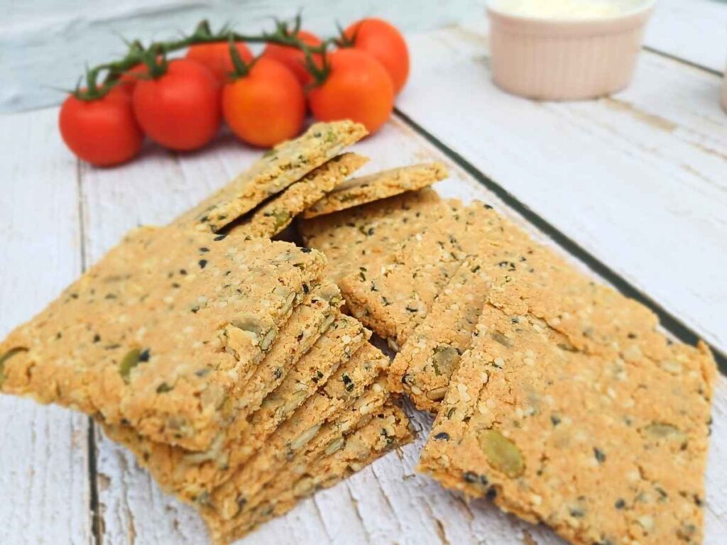 A pile of almond flour crackers with cherry tomatos in the background