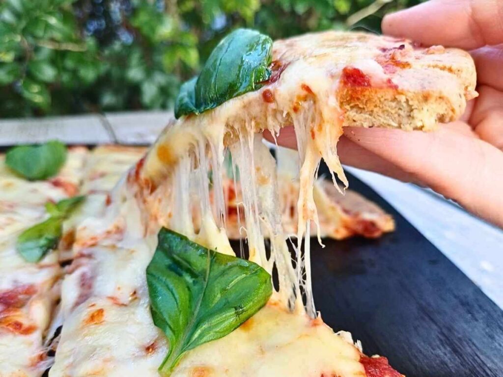 A slice of almond flour pizza crust topped with melted cheese and fresh basil