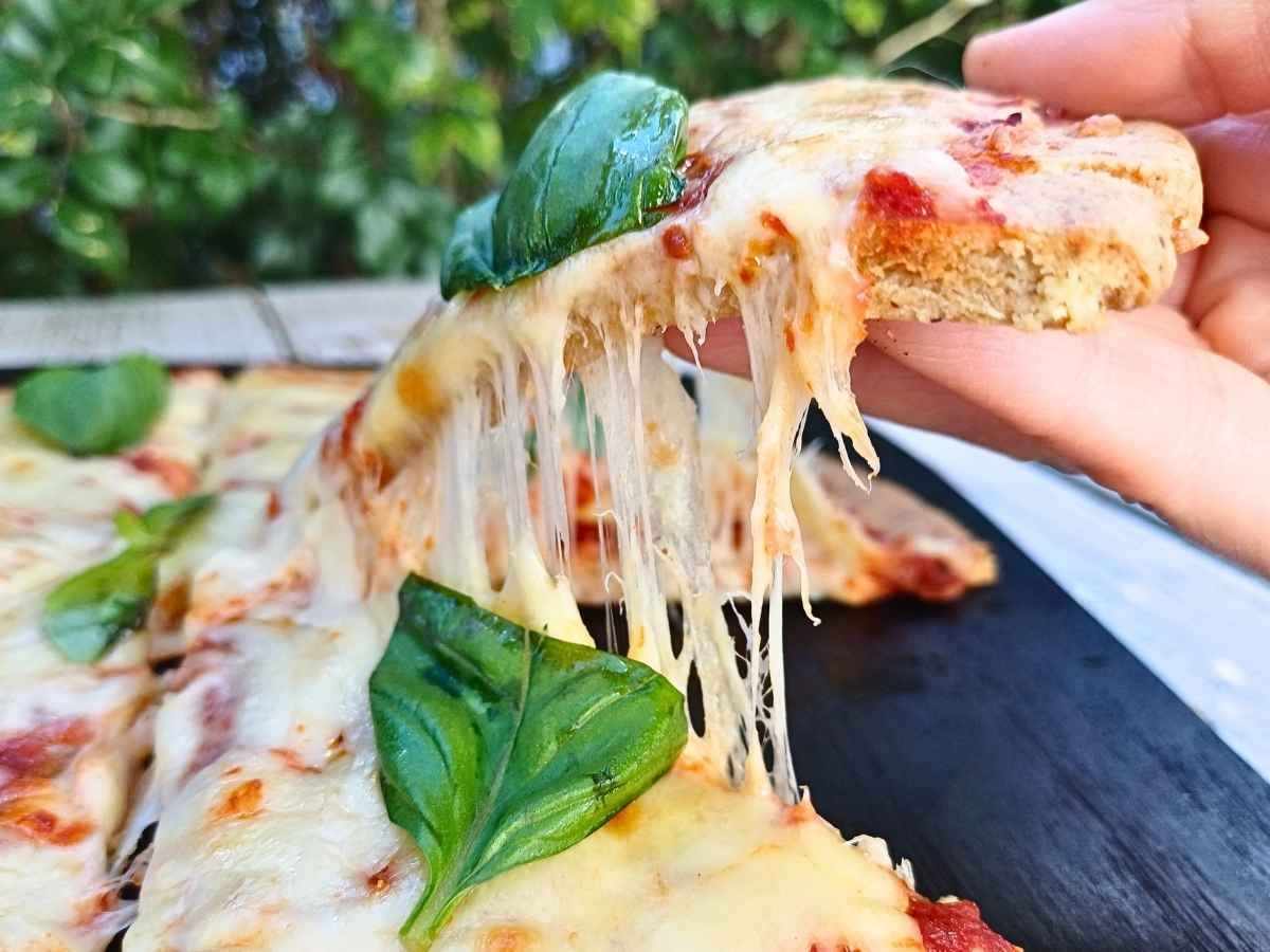 A slice of almond flour pizza crust topped with melted cheese and fresh basil