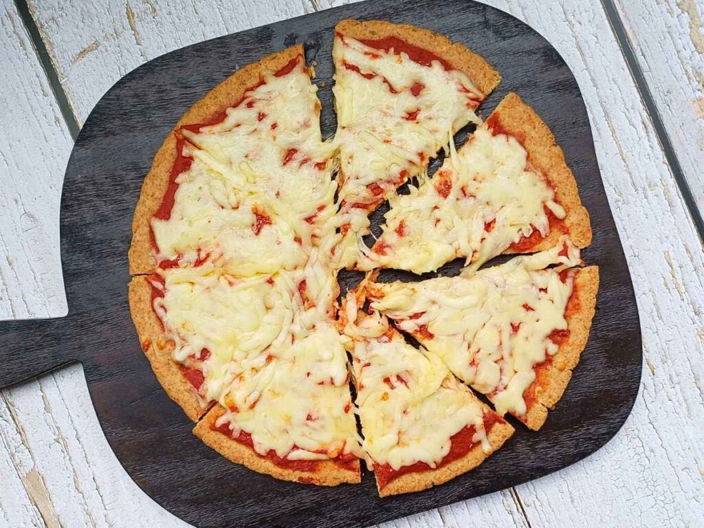 Almond flour pizza crust with cheesy topping on a dark board