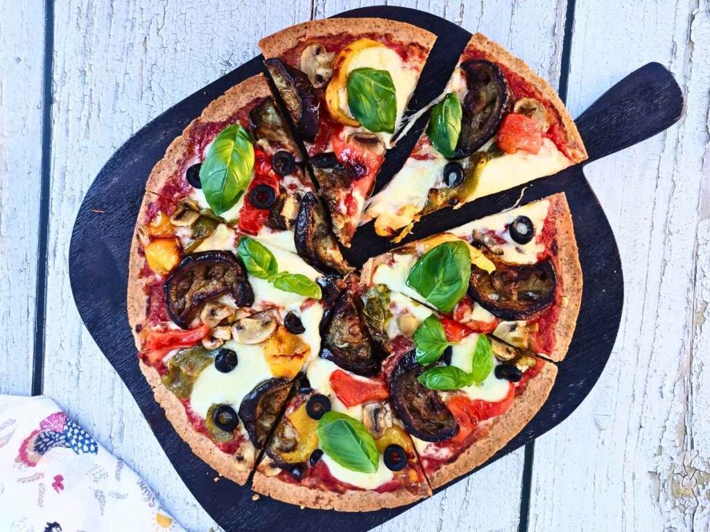 Vegetarian almond flour pizza with roasted vegetables and fresh basil leaves