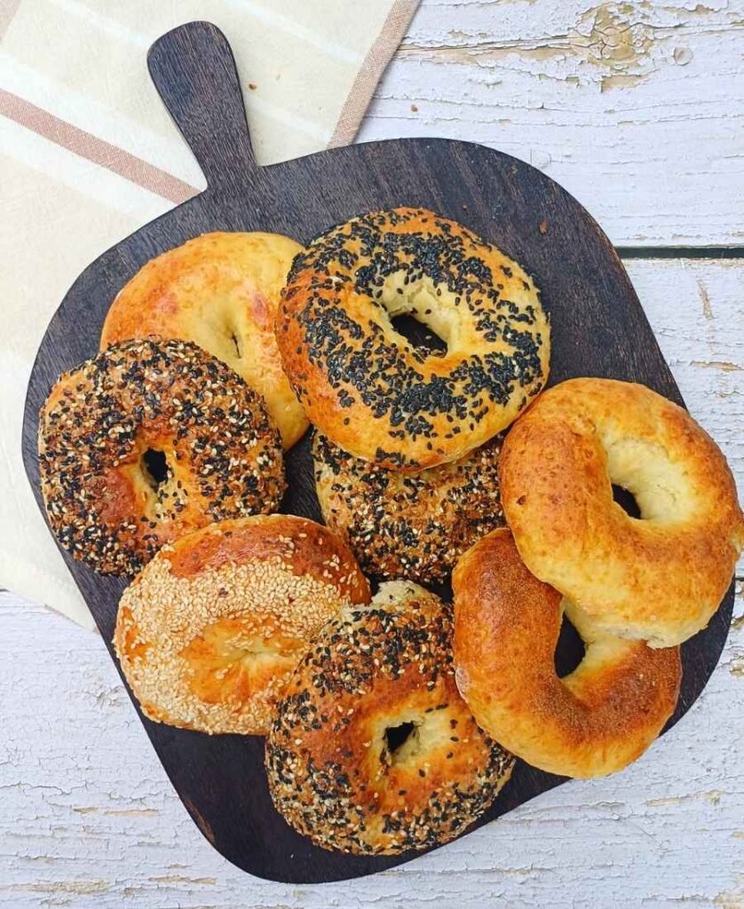 A stack of golden cottage cheese bagels on a dark wooden board with seasonings